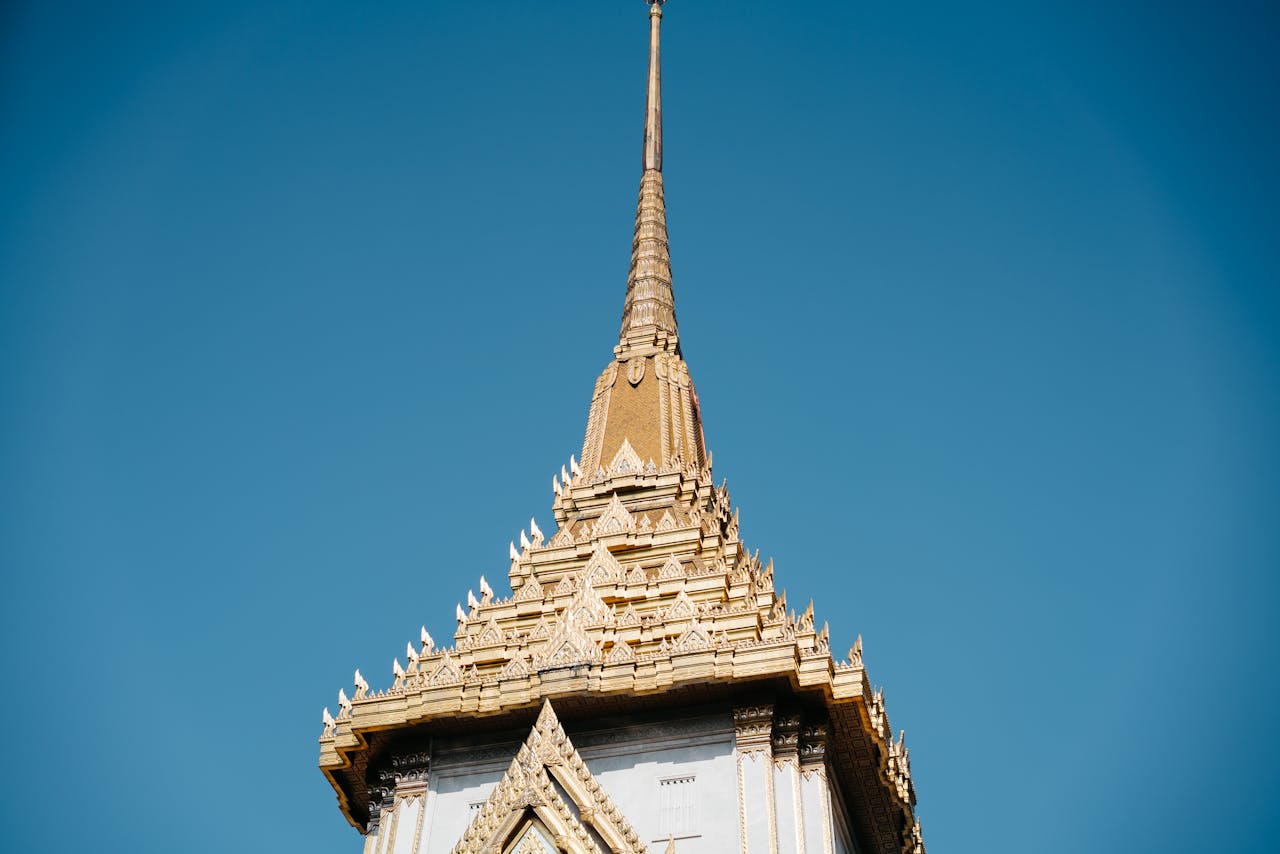 services-03 Low angle view of the golden spire of Wat Traimit temple in Bangkok under a clear blue sky.