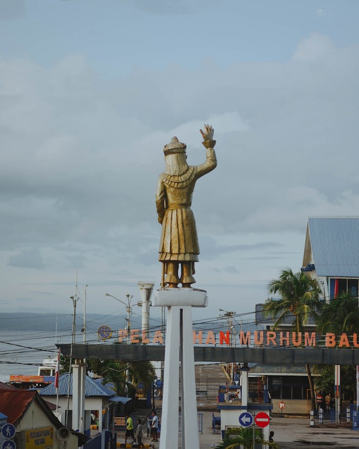 our-story Golden statue stands tall at port entrance with ocean view and cloudy sky.